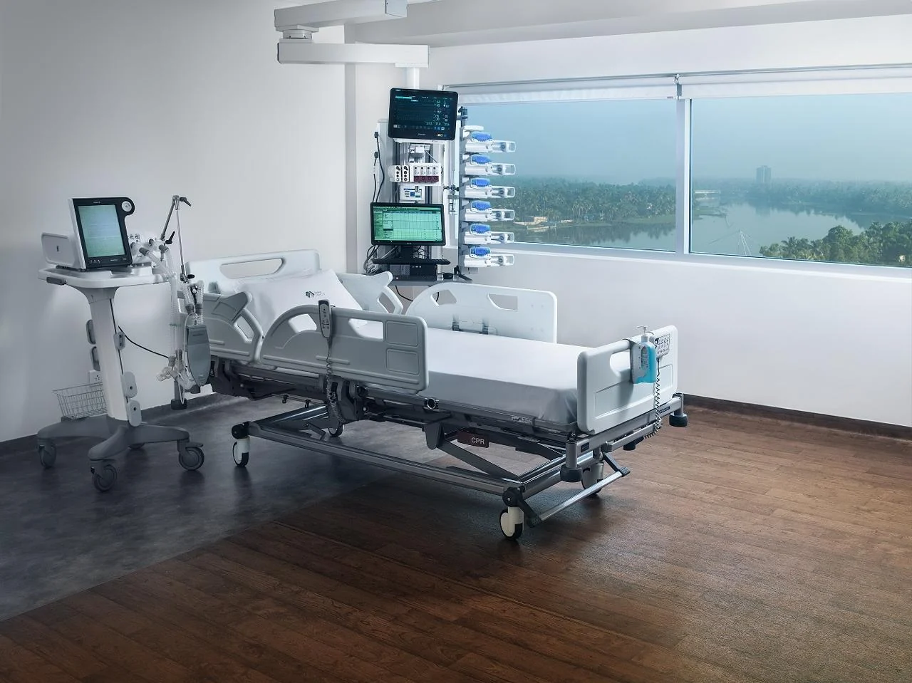 Critical-care bed with bedside monitoring and medical equipment beside a window