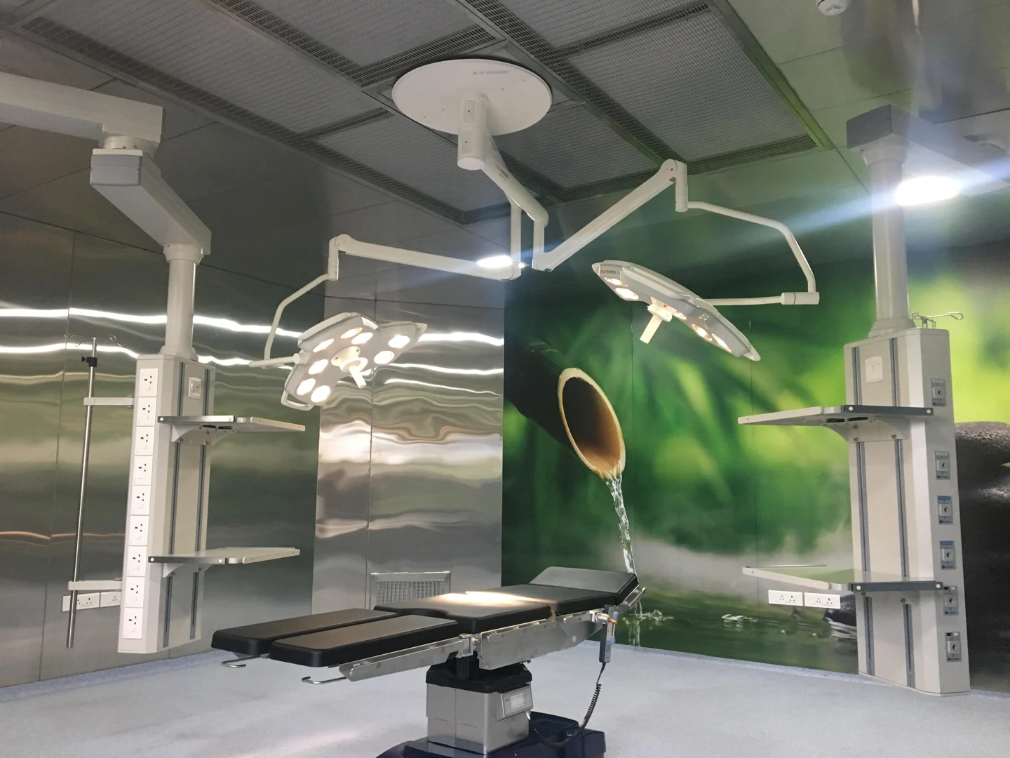 Operating theatre with a green wall mural, twin surgical lights and ceiling-mounted pendants